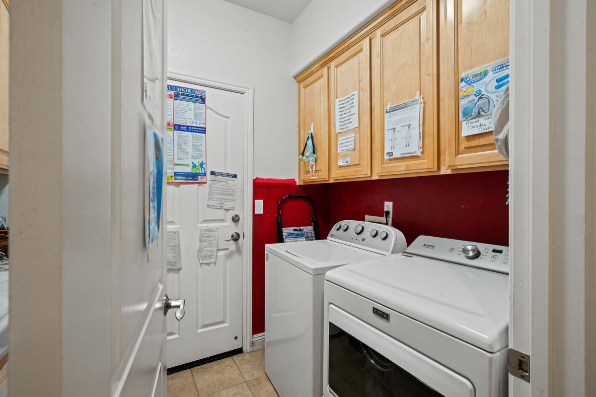 A small laundry room with a washer, dryer, and wooden cabinets.