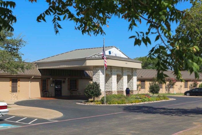 A building with an entrance surrounded by trees and a flagpole near the road.