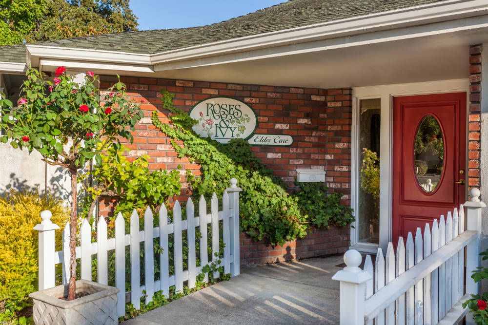 A charming brick house with a white picket fence and a red front door, adorned with greenery.
