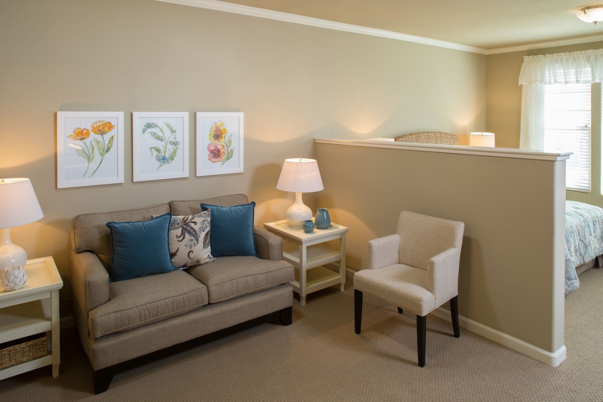 A cozy living room with a sofa, armchair, table lamp, and wall art.