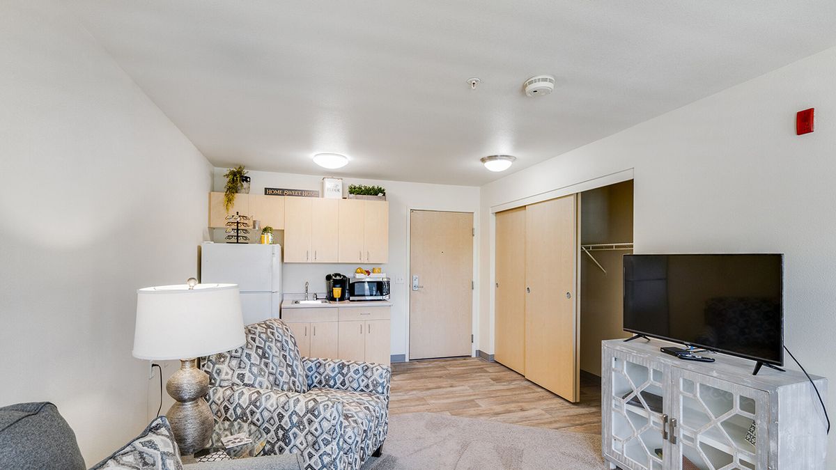 A modern apartment interior featuring a cozy living room with patterned furniture and a compact kitchenette.
