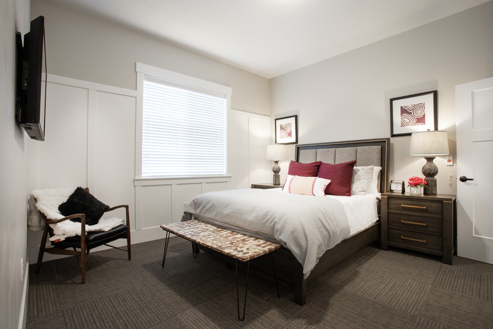A modern bedroom interior featuring a stylish bed with pillows, nightstands with lamps, and wall art.
