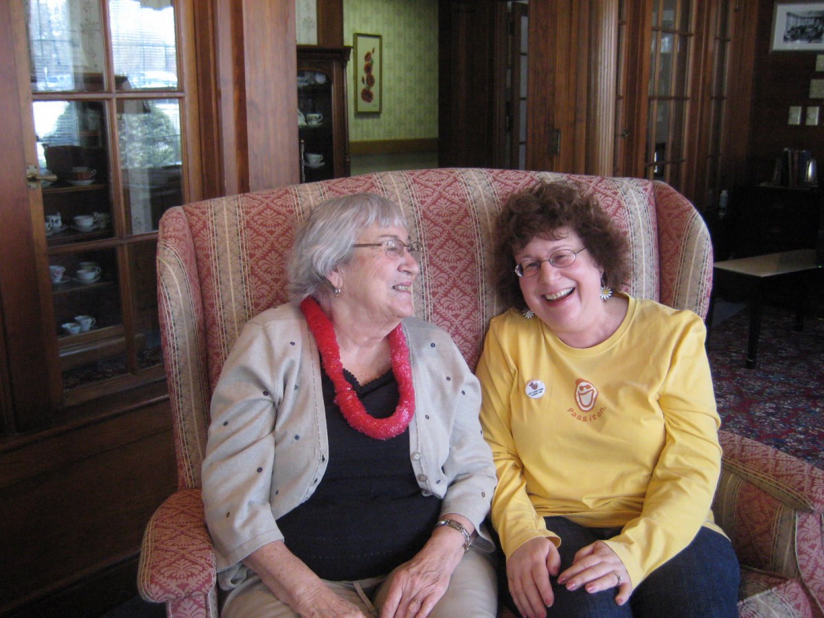 Two women sitting together, sharing a joyful conversation indoors.