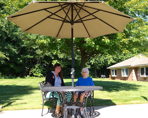 Two individuals enjoying a sunny day under an umbrella, engaged in conversation at a table.