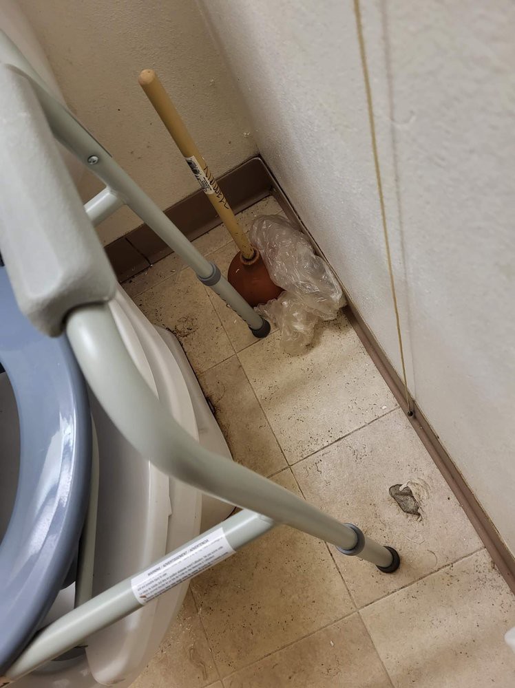A bathroom scene with a walker, a plunger, and tissue on the floor.