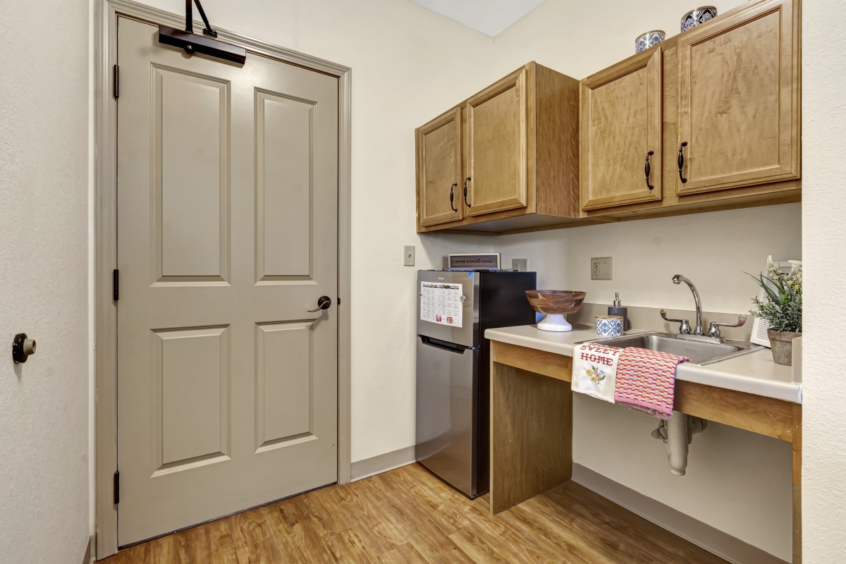 A compact kitchenette featuring a mini fridge, sink, and wooden cabinets.