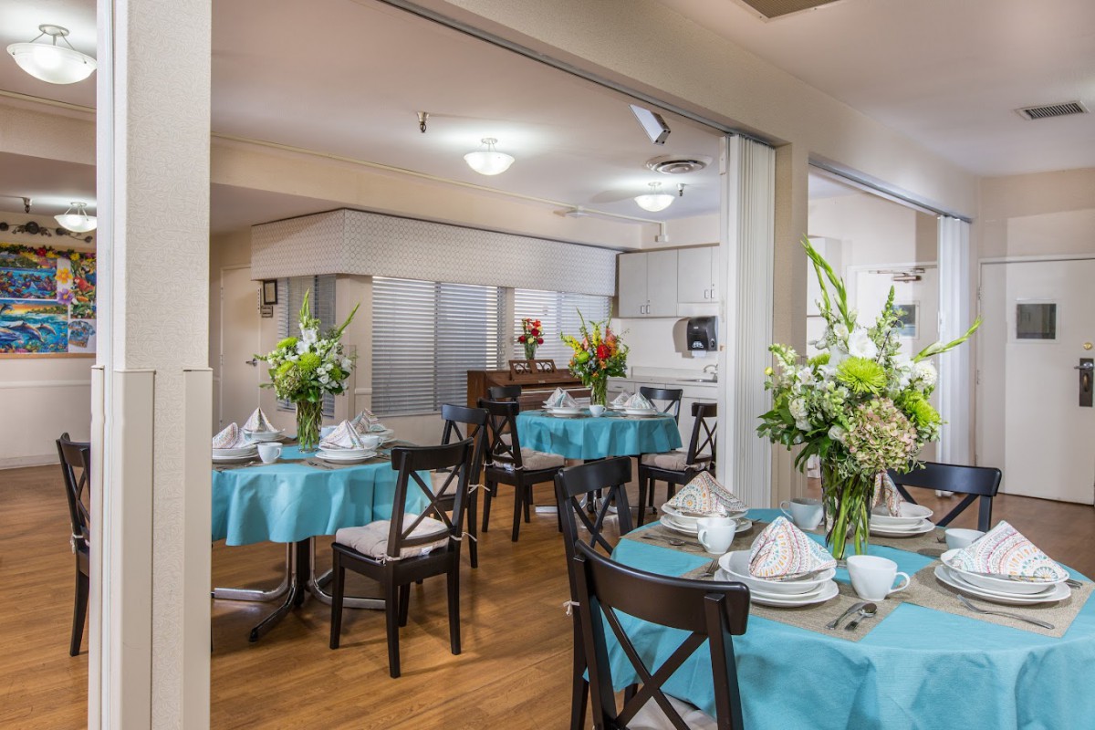 A well-decorated dining area with tables set for a meal, featuring floral arrangements and blue tablecloths.