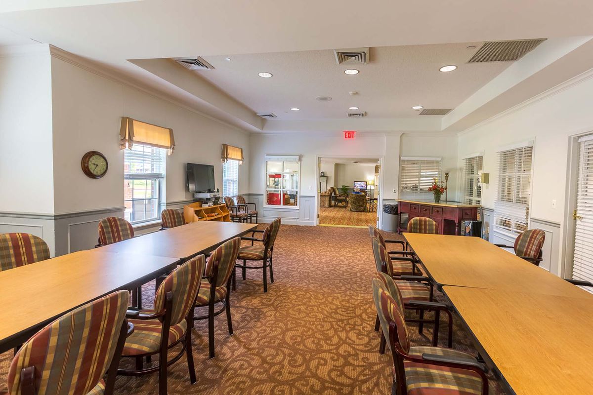 A spacious dining area with long tables, chairs, and large windows allowing natural light.