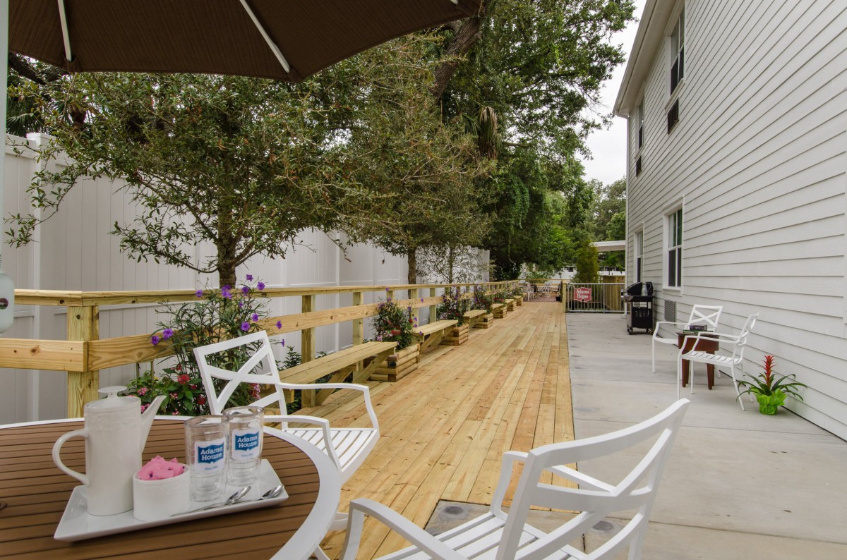 A spacious outdoor patio with white chairs and a wooden deck, surrounded by trees.