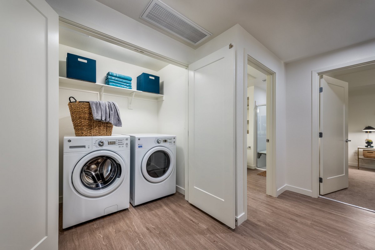 A modern laundry room with a washer and dryer, featuring storage shelves with baskets and a hardwood floor.