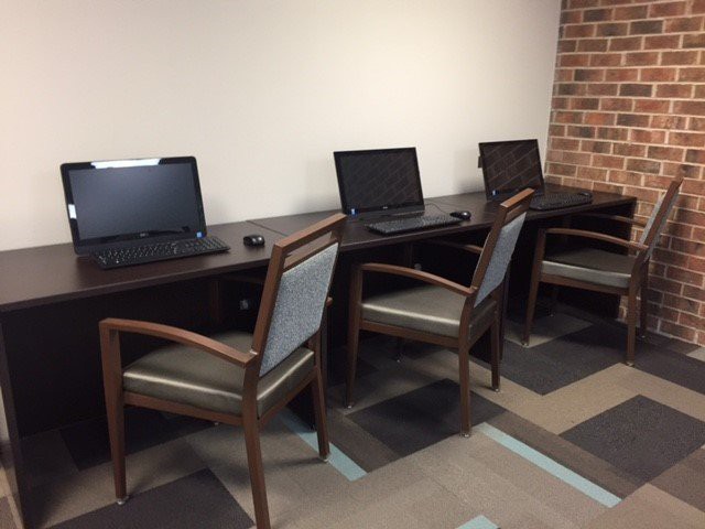 A row of workstations with computers and office chairs arranged in a modern workspace.