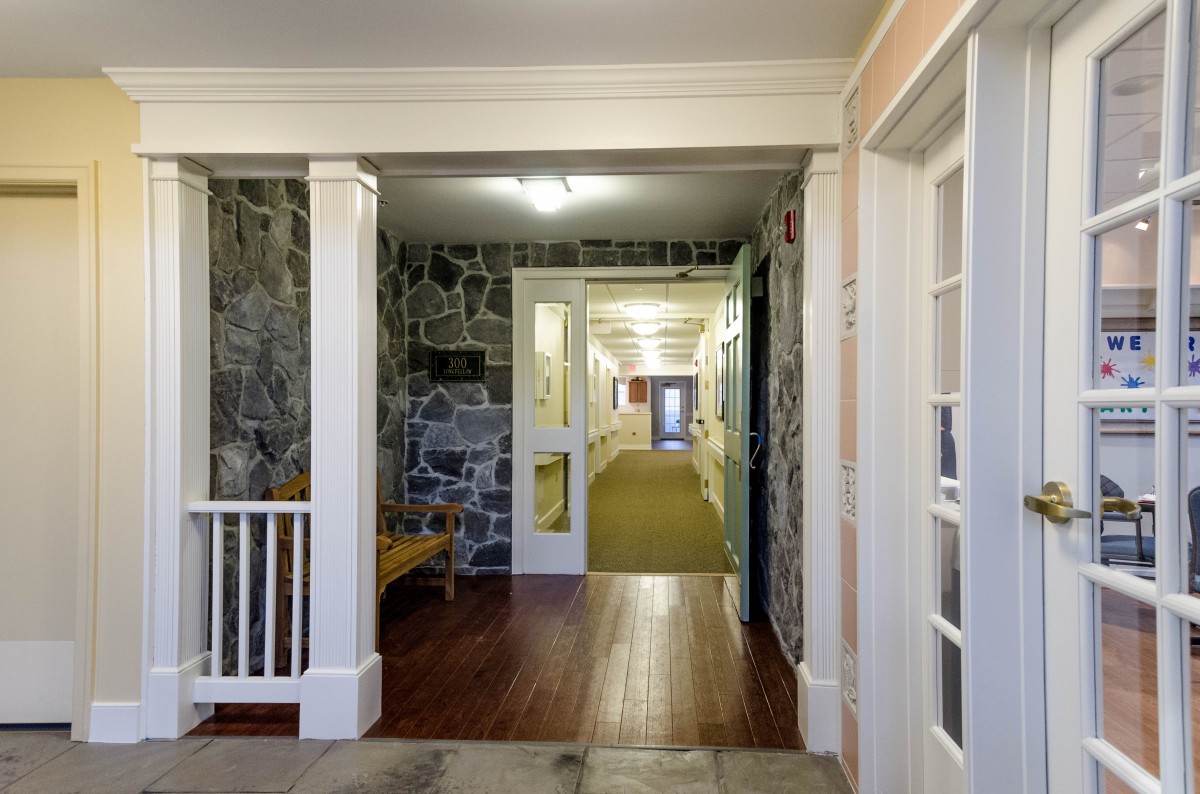 A well-lit hallway with stone walls, featuring a wooden floor and white doors leading to various rooms.