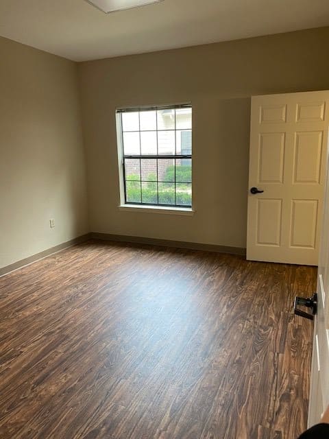 An empty room with wood flooring, a window, and a door.