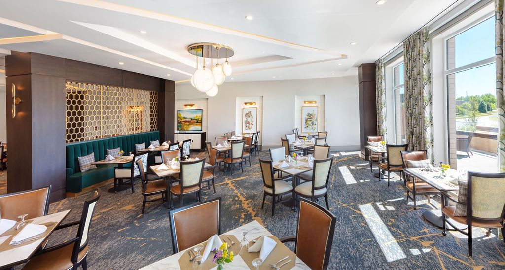 Elegant restaurant dining area with neatly arranged tables and chairs, featuring modern chandeliers and artwork on the walls.