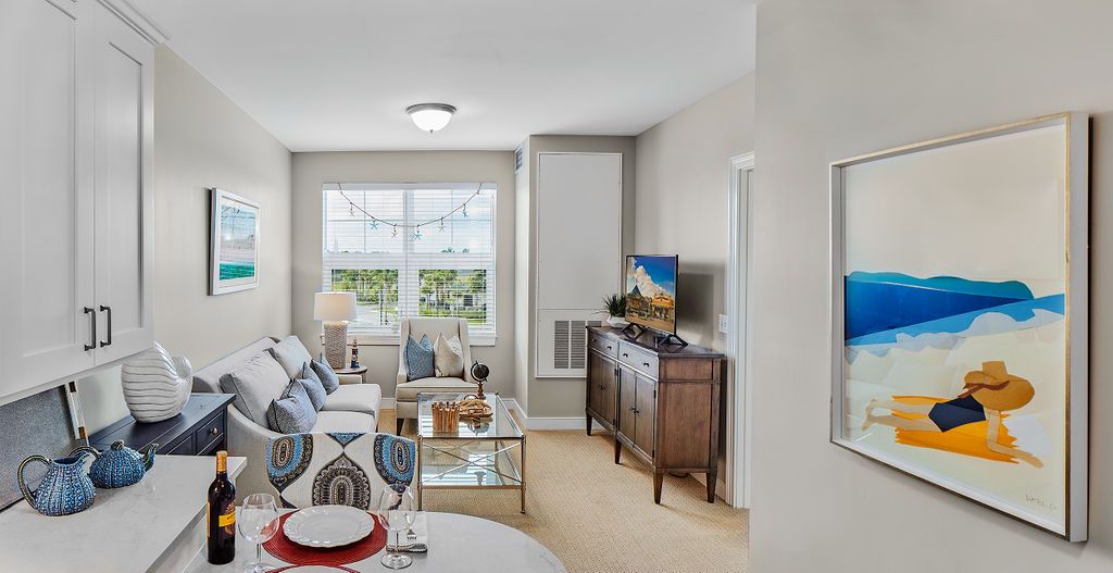 A cozy and well-decorated living room with a sofa, TV, coffee table, and large window providing natural light.