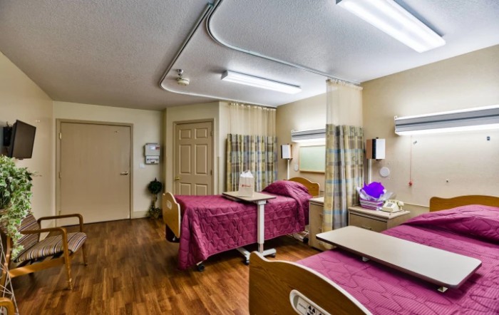 A healthcare facility room with two beds, separated by curtains.