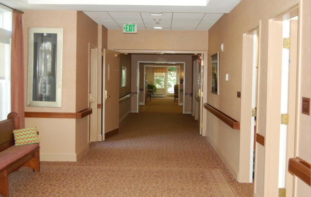 A long hallway in a building with open doors, carpeted floor, and handrails along the walls.