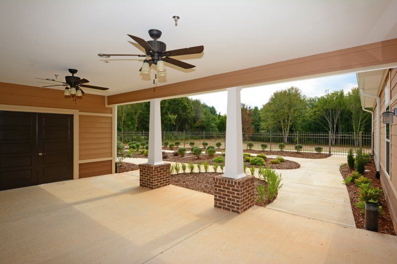 A spacious porch with ceiling fans overlooks a landscaped garden and driveway.