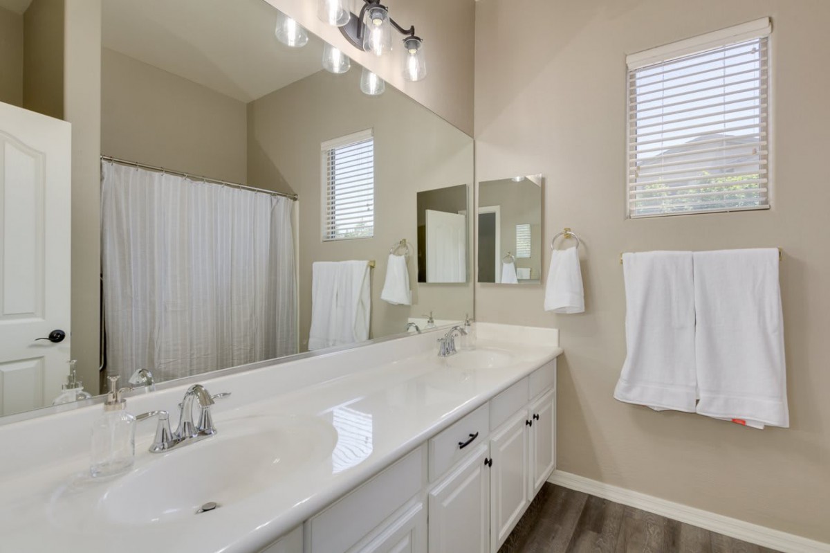 A modern bathroom featuring a large vanity with dual sinks, mirrors, and a light fixture, complemented by a shower area and neatly hung towels.
