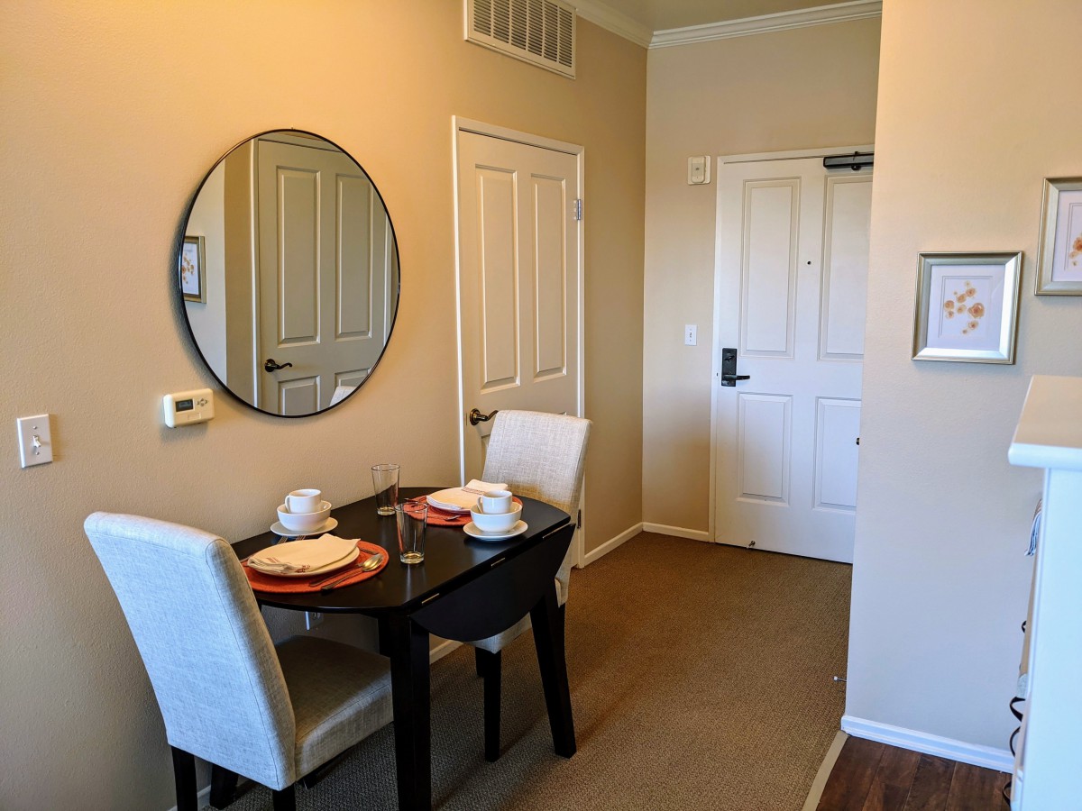 A cozy dining area with a small table set for two, featuring a round mirror on the wall.