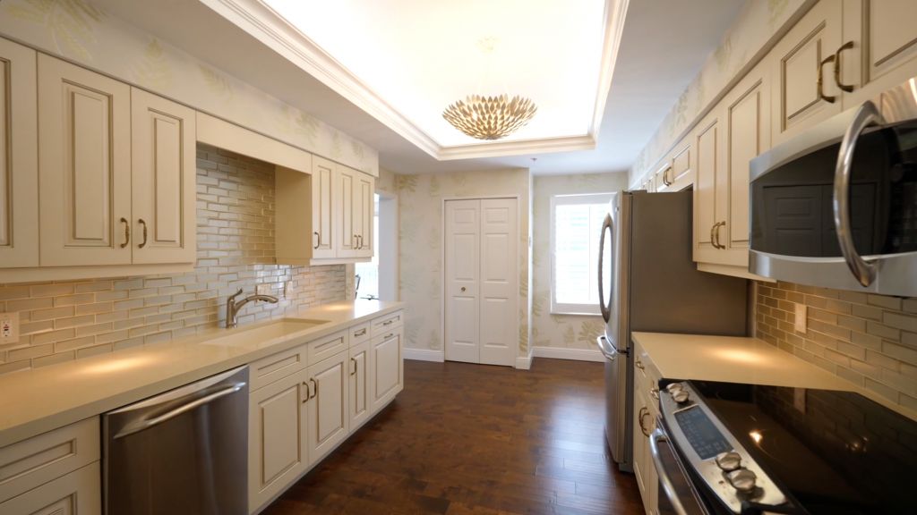 A modern kitchen with white cabinets, wood flooring, and stainless steel appliances.