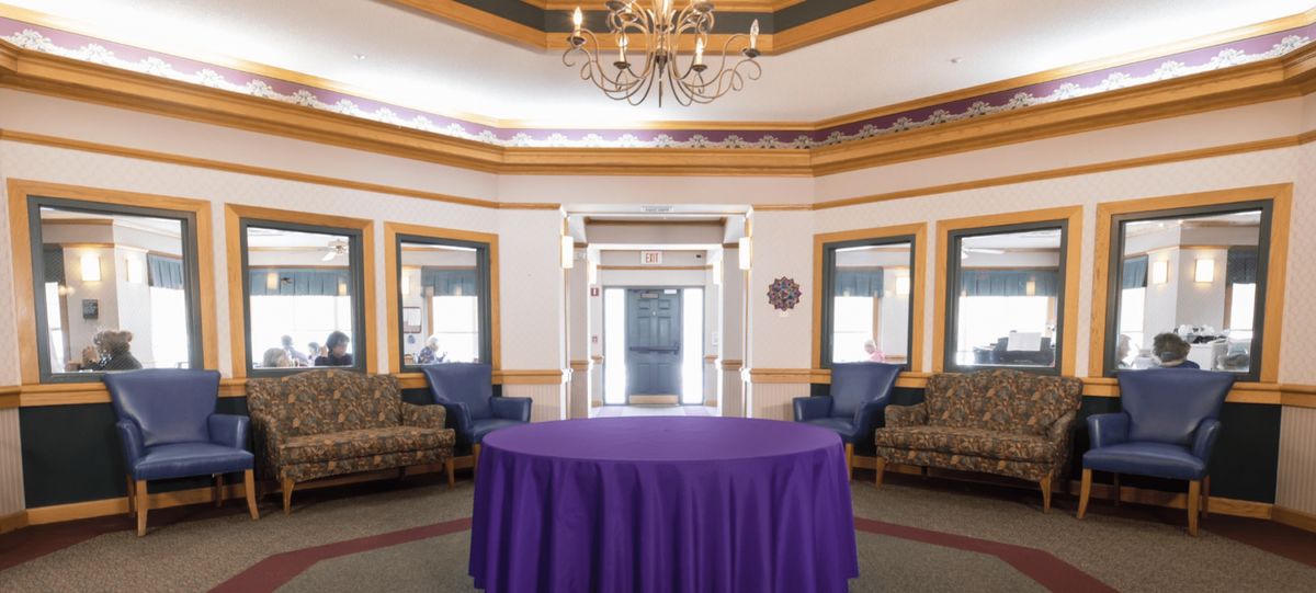 An elegantly decorated room featuring a purple tablecloth-covered table, surrounded by seating and lit by a chandelier.
