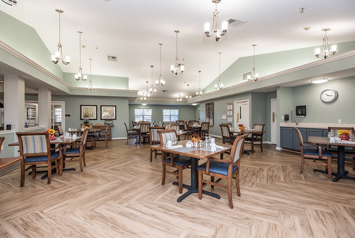 An elegant dining area featuring wooden flooring, neatly arranged tables and chairs, and stylish chandeliers.