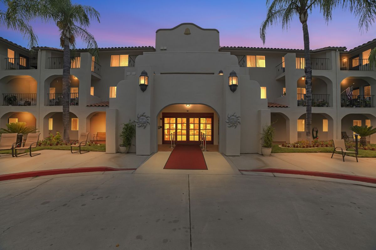 A beautifully lit hotel entrance with a red carpet driveway and palm trees at dusk.