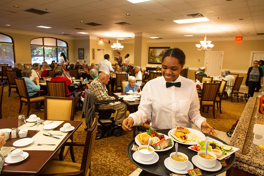 A waiter serves food to customers in a busy restaurant dining room.