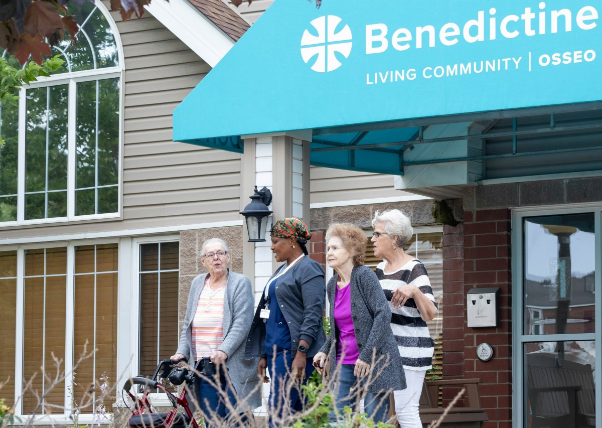 A group of seniors with a caregiver outside a nursing home called Benedict Living Community.