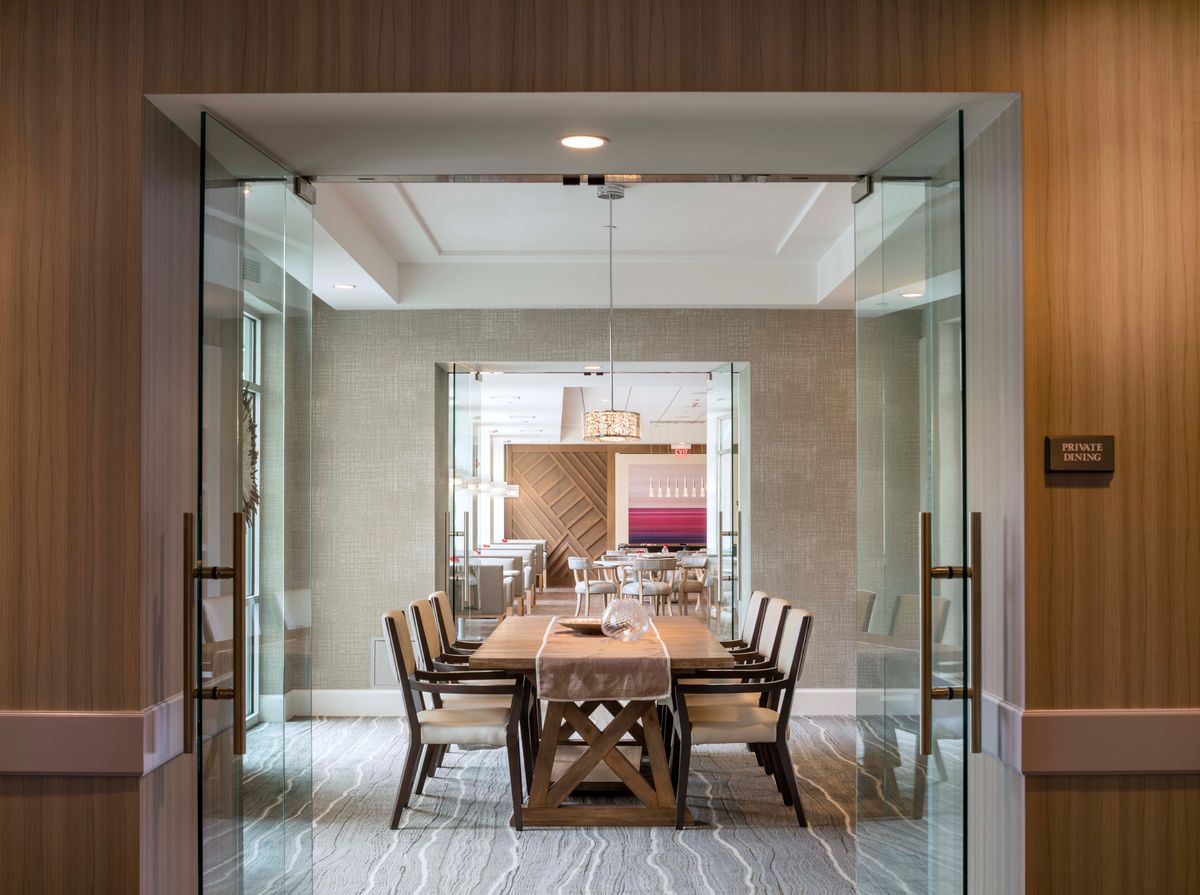 A modern dining room with a wooden table and chairs, enclosed by glass doors.