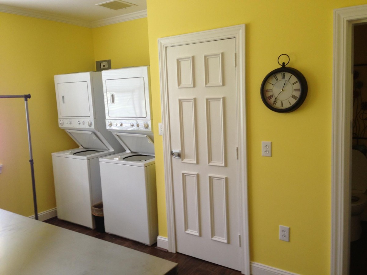 A bright laundry room with yellow walls, featuring a washing machine and dryer, alongside a wall clock.