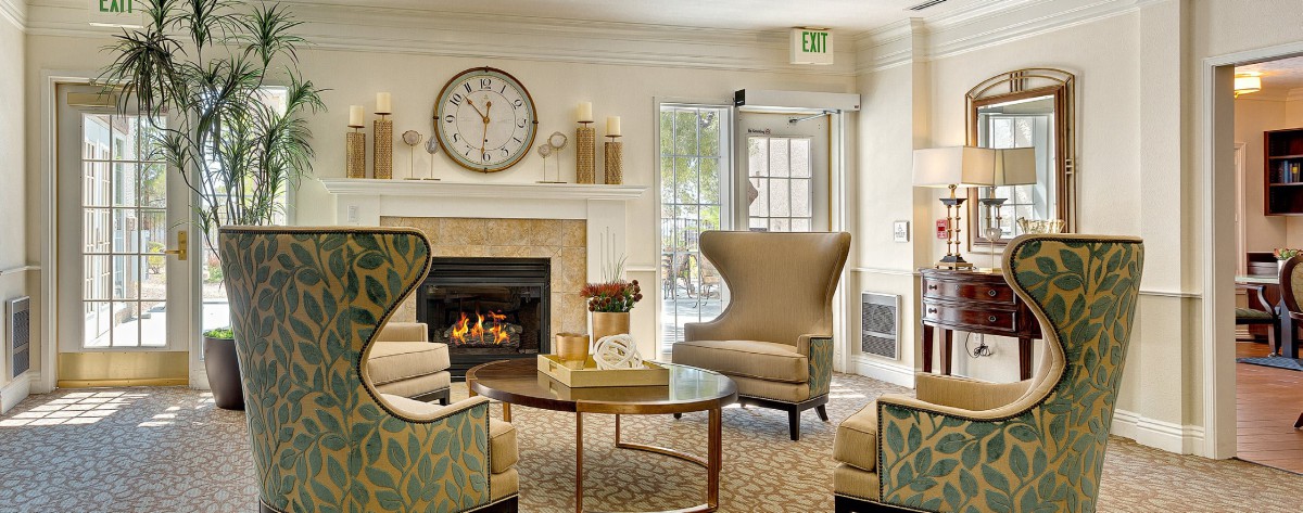 A cozy living room with elegant seating around a fireplace, featuring stylish armchairs and a decorative wall clock.