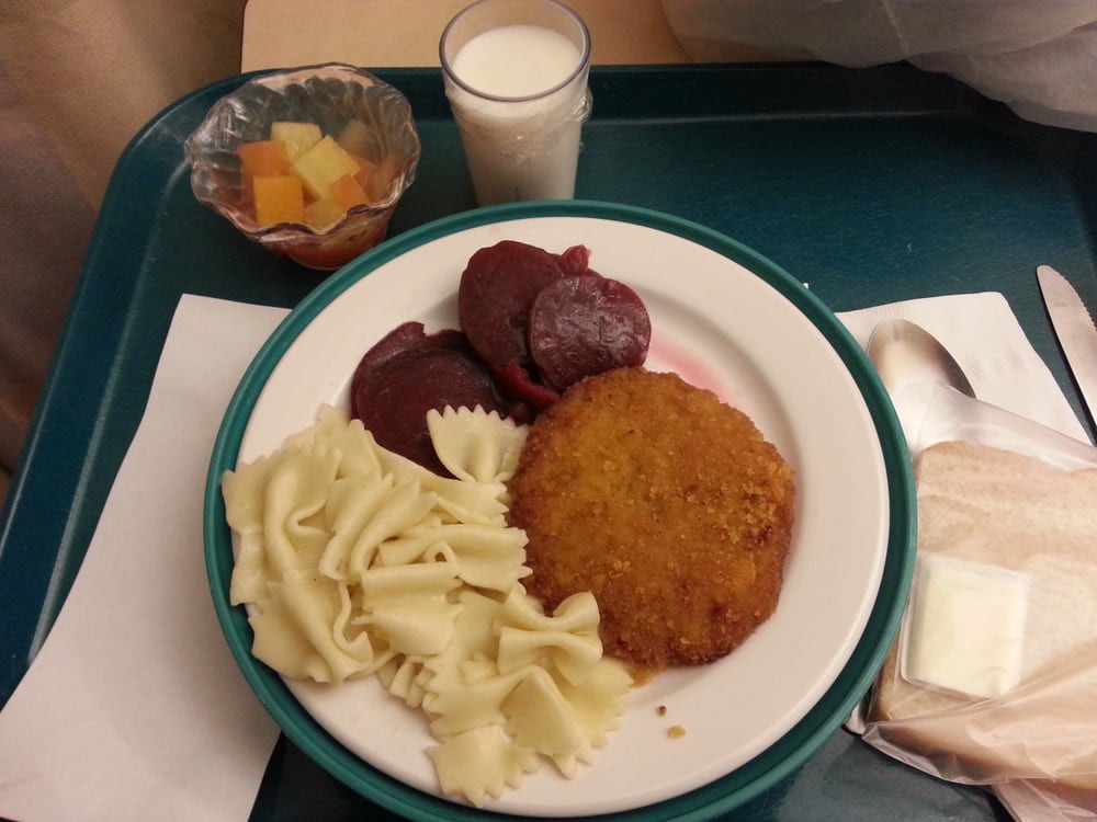 A meal served on a tray includes pasta, a fried cutlet, sliced beets, fruit salad, and a glass of milk.