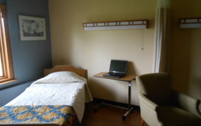 A minimalist hospital room with a bed, chair, and a small desk.