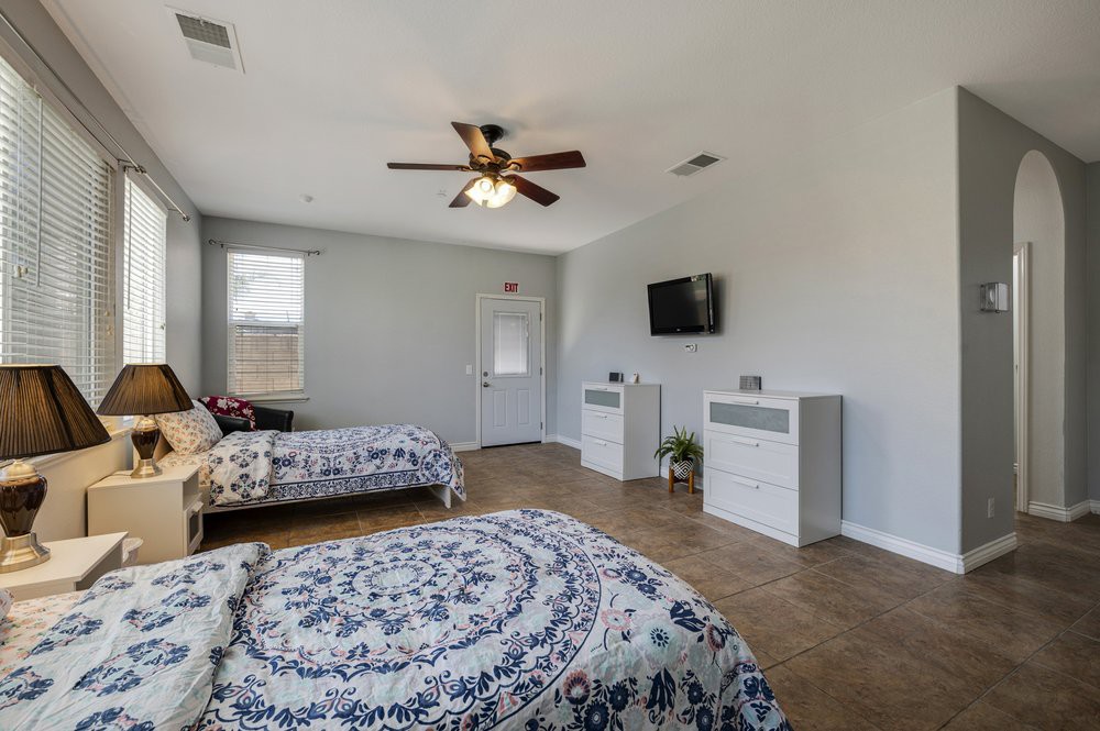 A spacious bedroom with two beds, a ceiling fan, and a mounted TV.