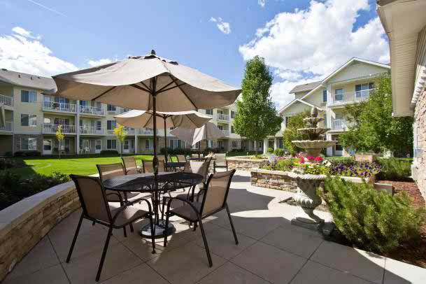 A sunny outdoor patio area with tables, chairs, and umbrellas in a well-landscaped garden setting.