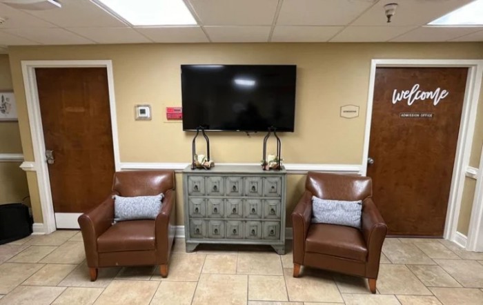 A waiting room with two leather chairs, a console table, and a mounted television on the wall.