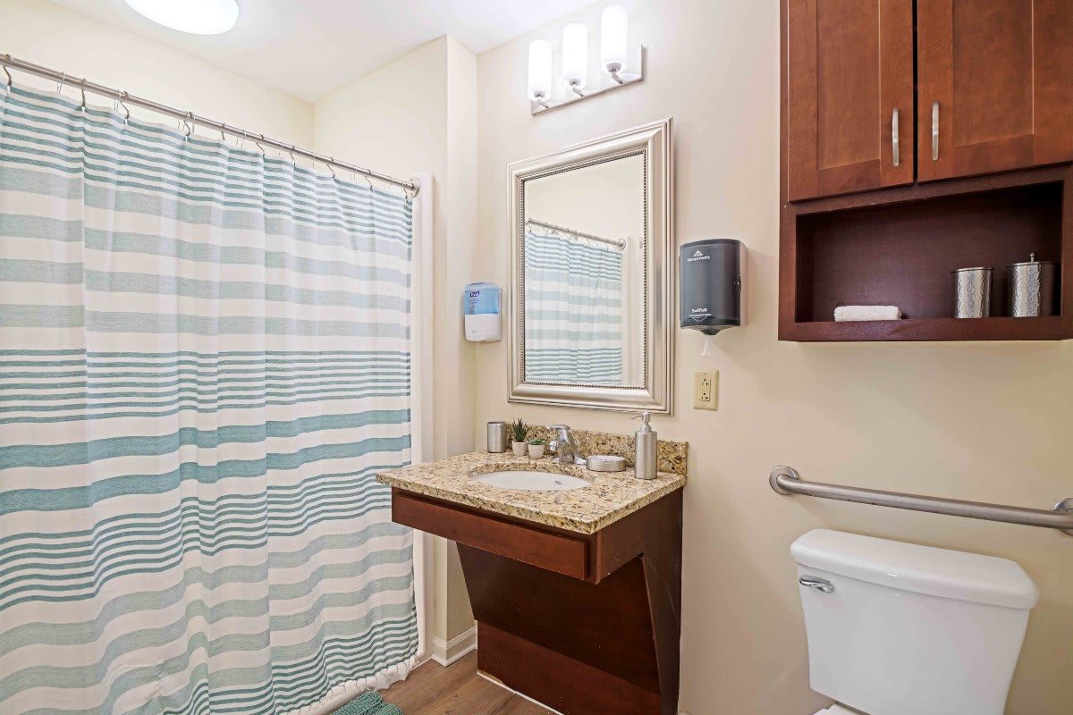 A modern bathroom featuring a sink with a mirror, striped shower curtain, and wooden cabinetry.