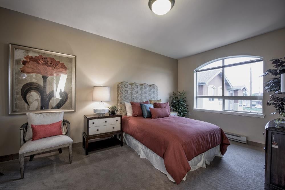 A cozy and elegantly decorated bedroom featuring a comfortable bed, nightstand with a lamp, and large window.