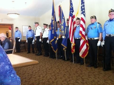 An honor guard stands in formation indoors, holding flags, including the American flag.