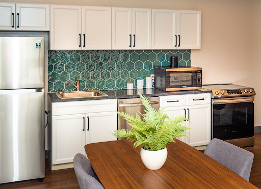 A modern kitchen featuring a green hexagonal backsplash, white cabinets, and a cozy dining area.
