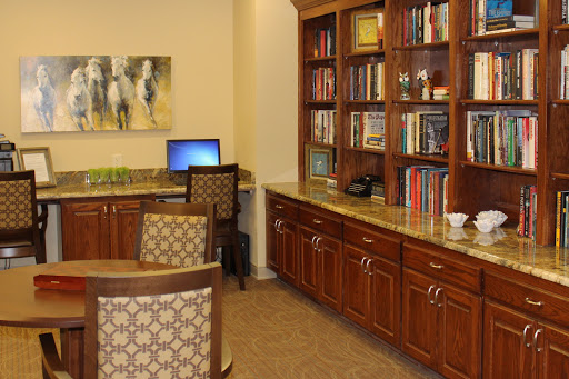 A cozy office space featuring a wooden bookshelf filled with books, a computer setup, and comfortable chairs.