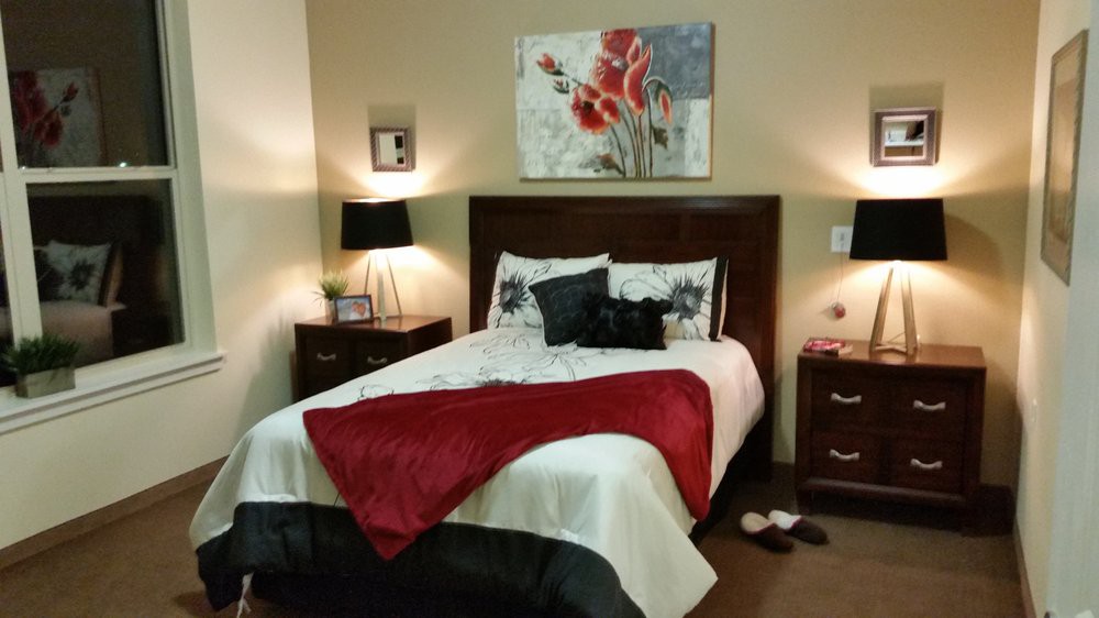 A cozy bedroom with a neatly made bed, featuring colorful artwork and decorative pillows.