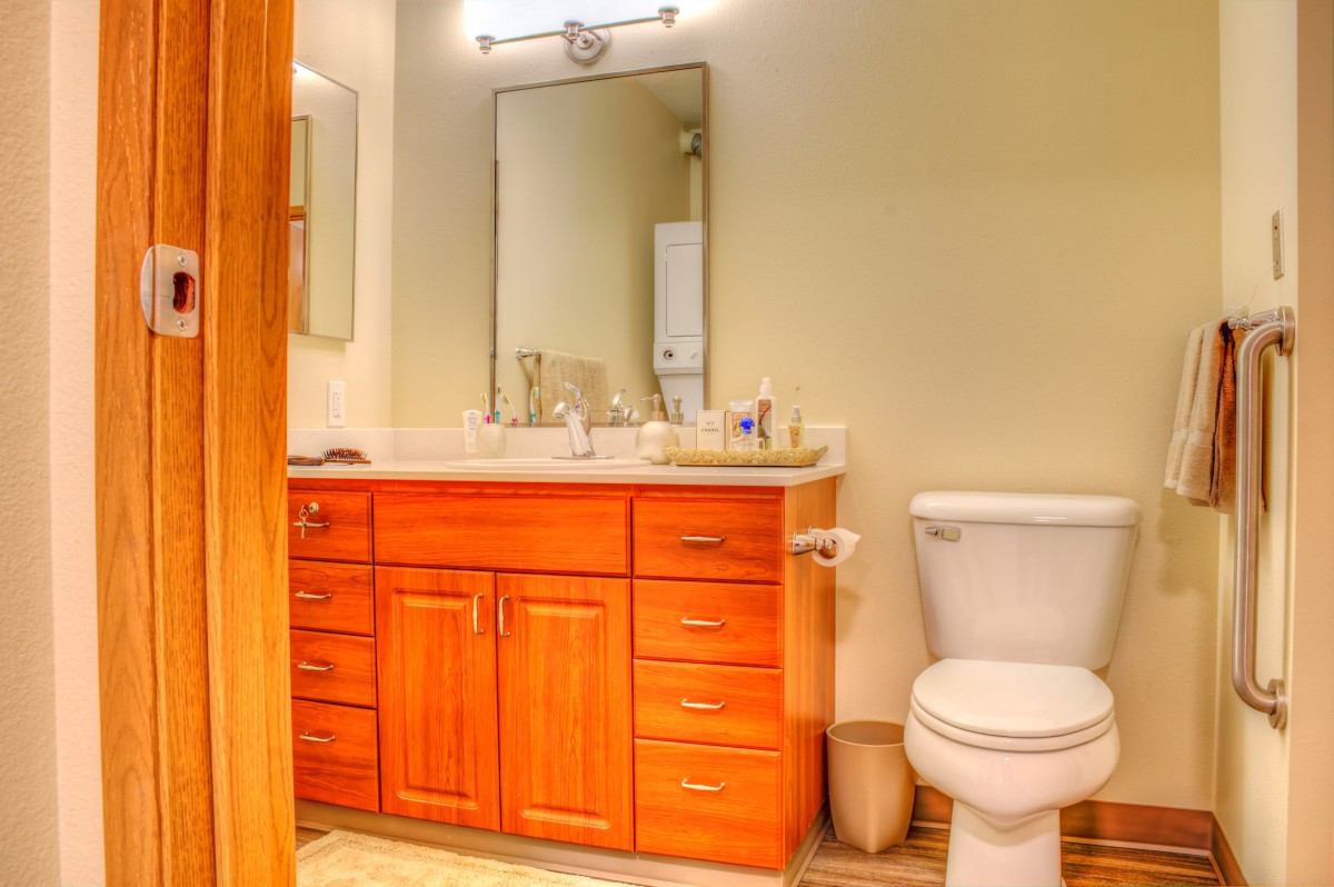 A well-lit bathroom with a wooden vanity, sink, and mirror next to a toilet.