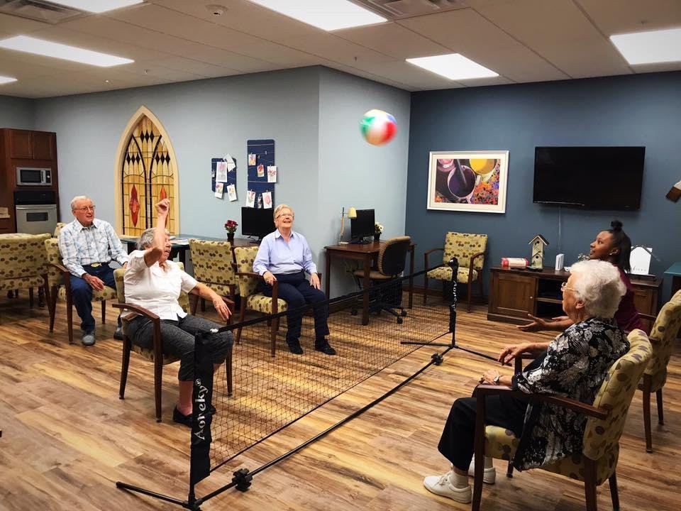 A group of seniors playing seated volleyball indoors using a beach ball.