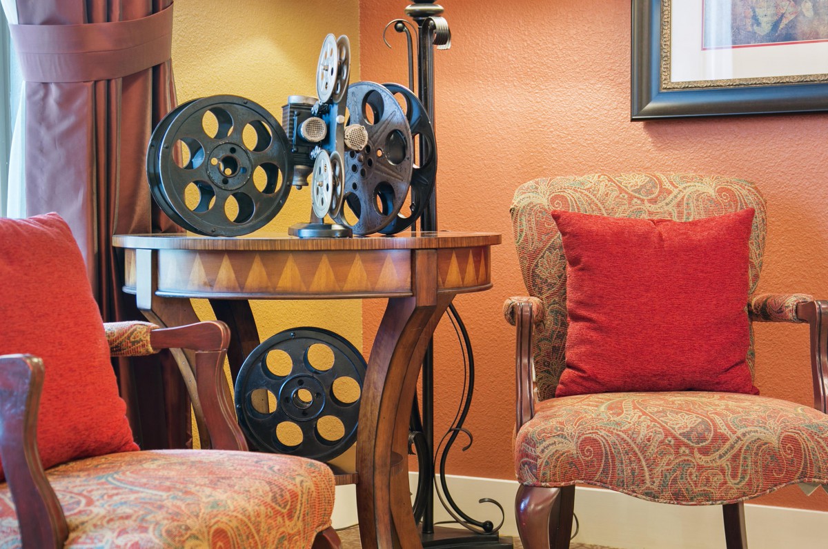 A cozy seating area featuring a vintage film projector on a wooden table, with plush armchairs and warm lighting.