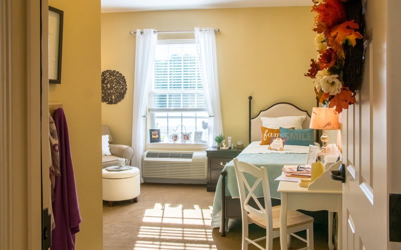 A cozy bedroom with a well-decorated interior featuring a comfortable chair, table, and bed by a window.