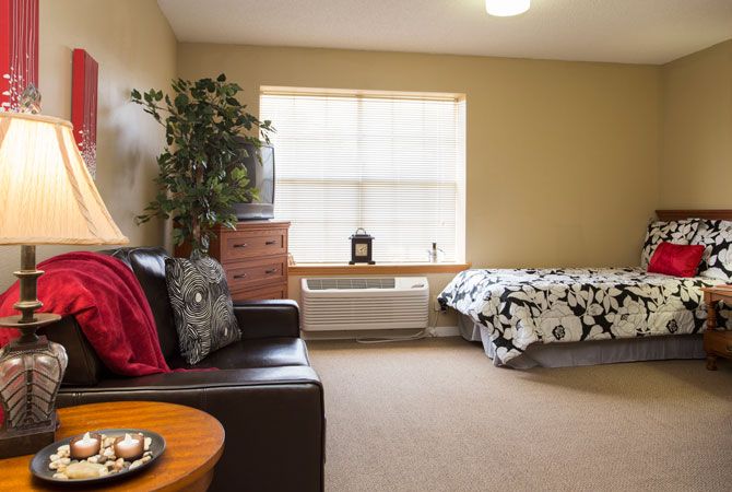 A cozy living space with a bed, sofa, and natural light from a large window.