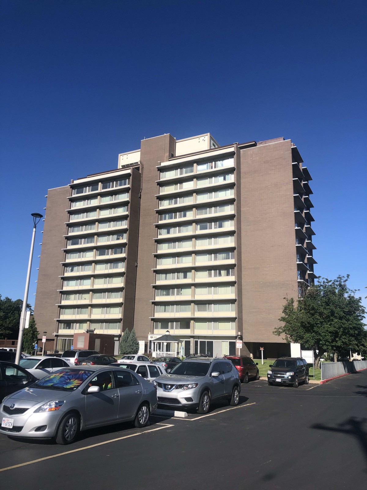 A high-rise apartment building with a parking lot in front, on a sunny day.